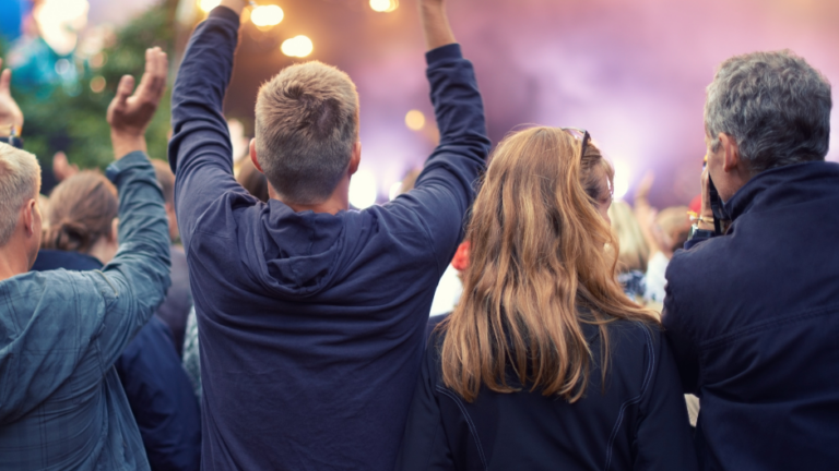 The back of four middle aged adults an an outdoor music event.