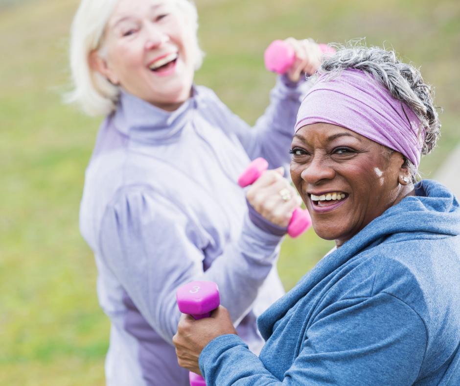 Two senior women lifting small pink weights outside to increase strength and prevent falls