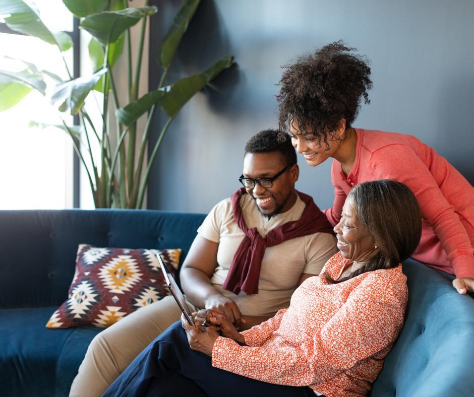 Elderly couple on couch looking at i-pad, young woman leaning over back of couch