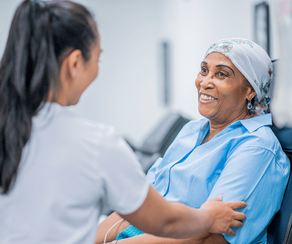 Female cancer patient sits in hospital chair while nurse gently touches her arm at Pacific Neuroscience Institute.