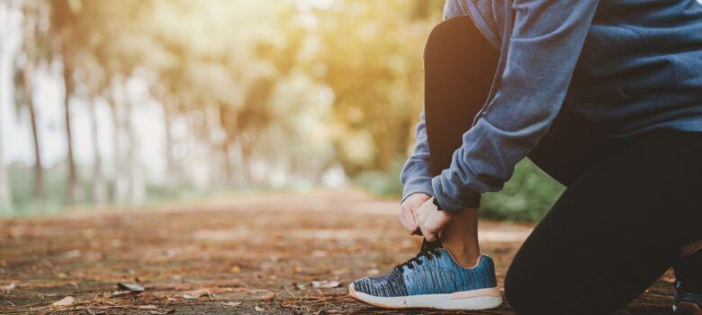 Person tying running shoes on a leaf-covered path in autumn, preparing for outdoor exercise.