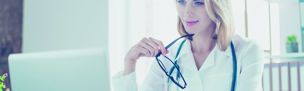 female physician working on a laptop holding her glasses