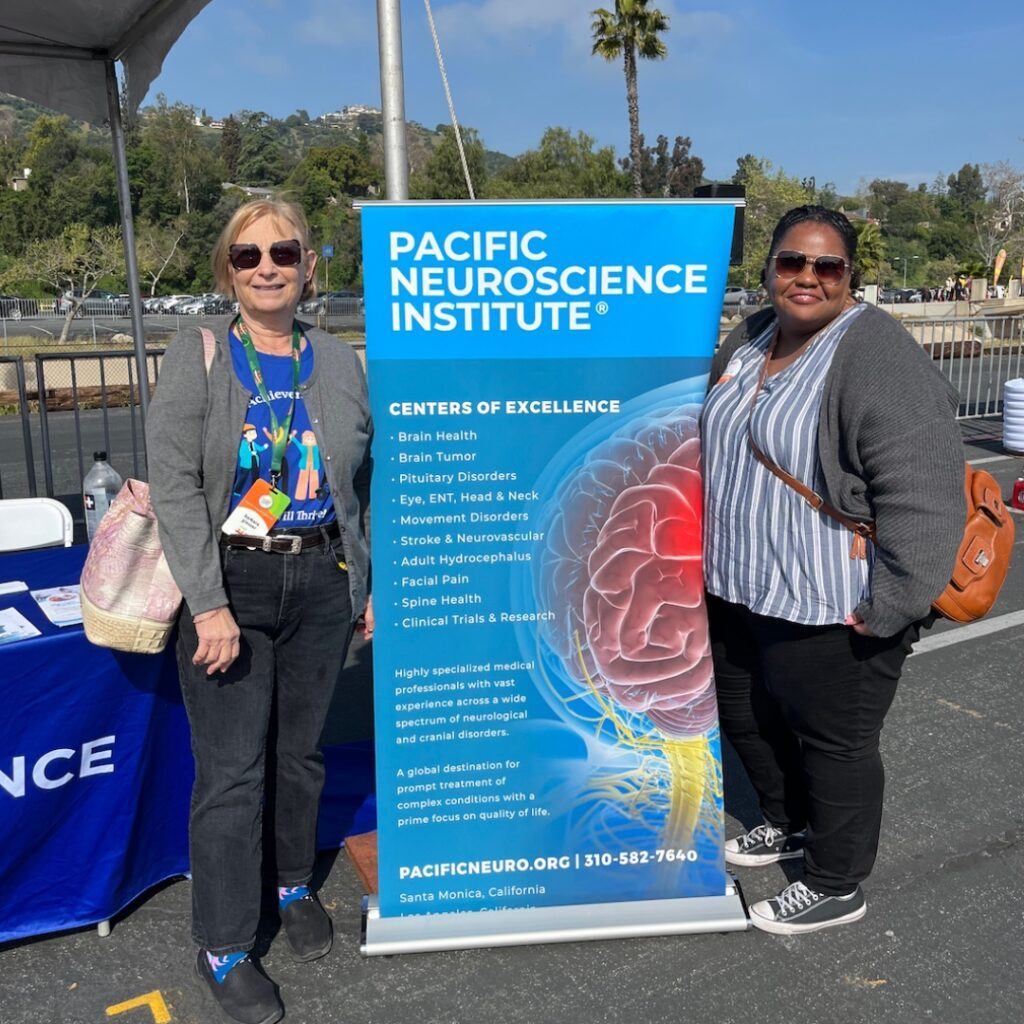 Barbara Giesser, MD, and Amber Henry stand next to the Pacific Neuroscience Institute's banner at Walk MS Los Angeles.